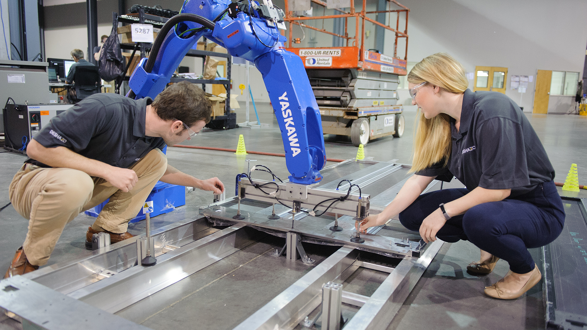 Two students and a machine work on a structure lying on the floor.