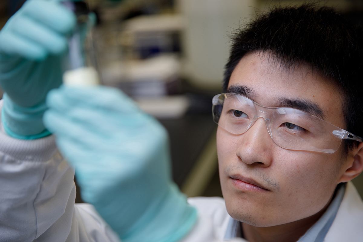 A student in protective gear studies a vial's contents.