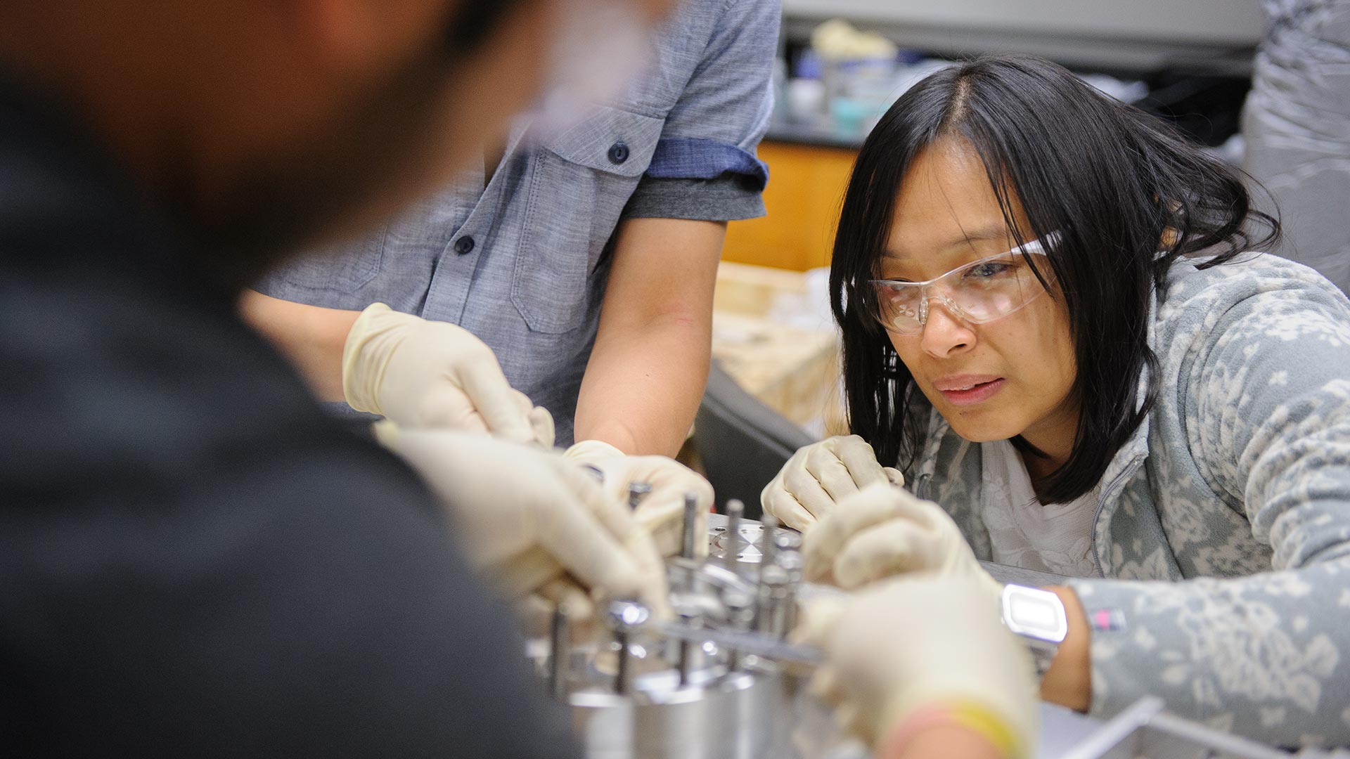 Close up of a woman working on machine parts in a group.