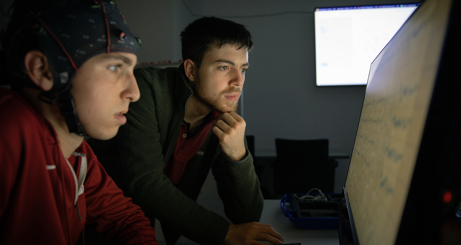 Students look at a computer screen with one wearing a monitering device on his head.