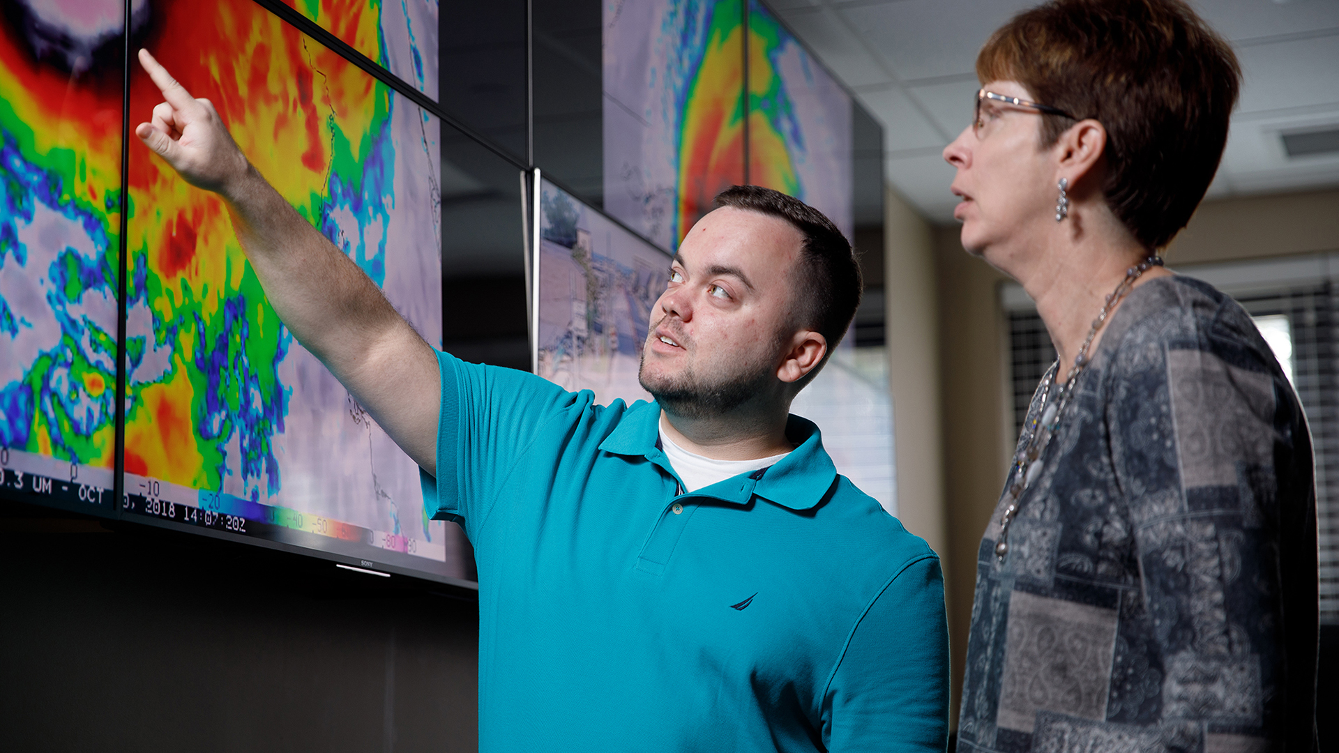 Two people look at a weather radar on screen.