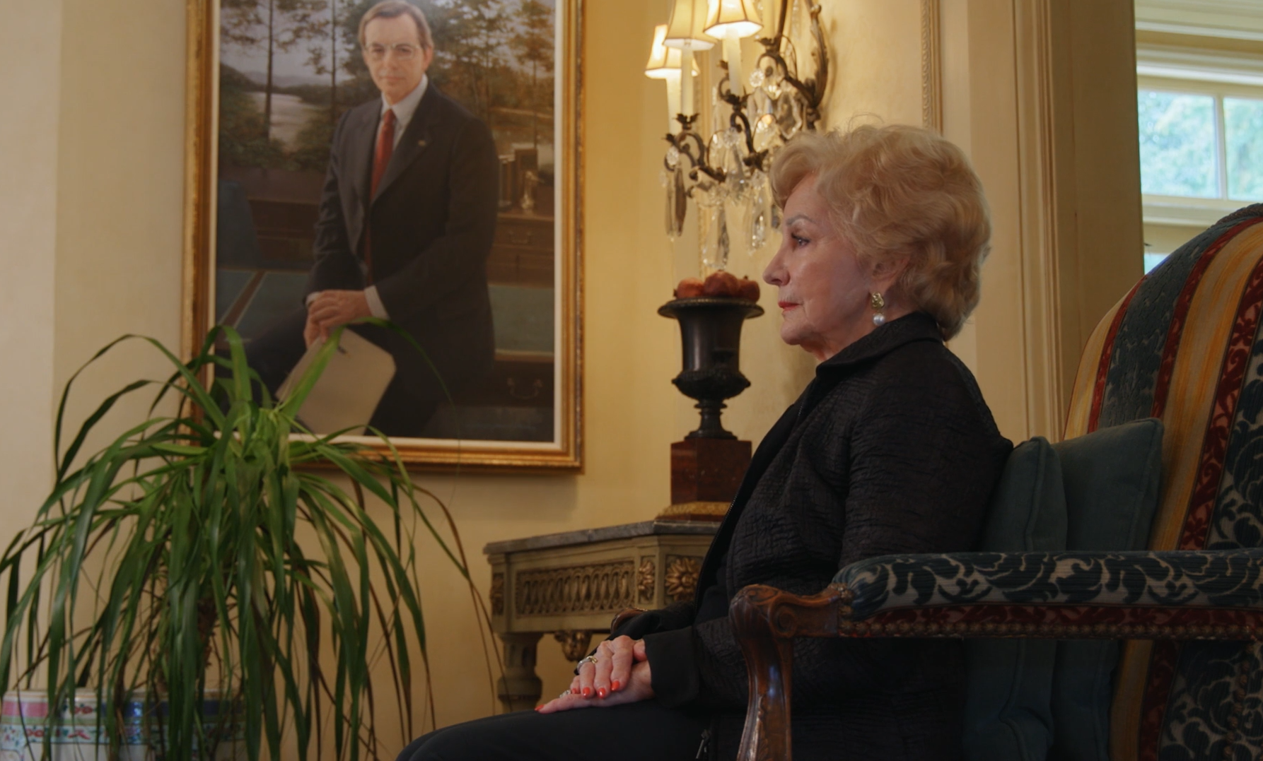 Mrs. Styslinger sitting with a painting of her husband in background